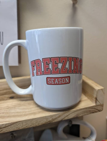 A white ceramic mug with freezing season printed on both sides in pink
